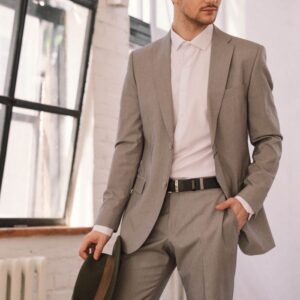 Elegant man in a gray suit holding a hat, posing indoors with a confident look.